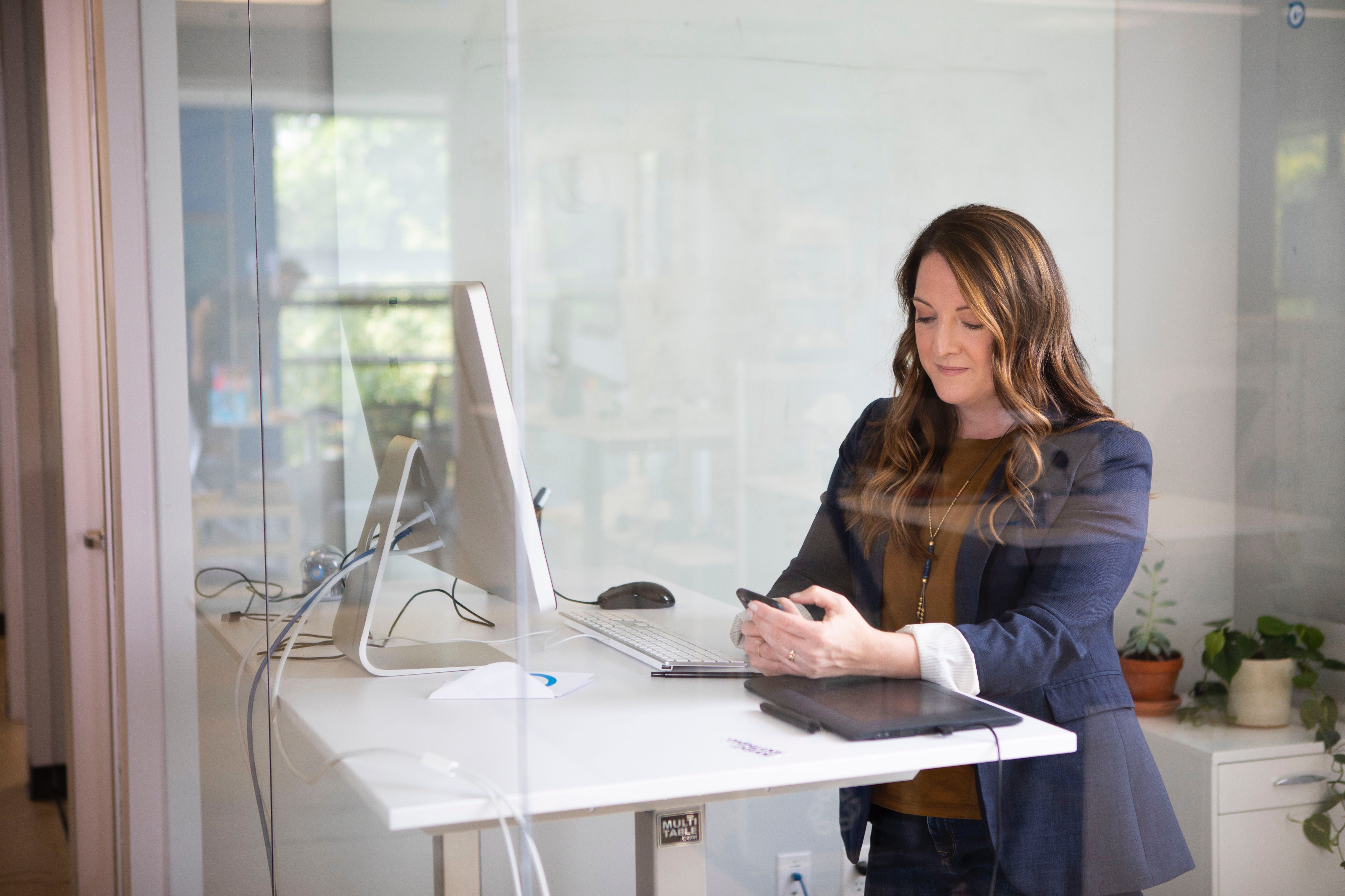 Woman standing up at desk in office with mobile phone in her hand